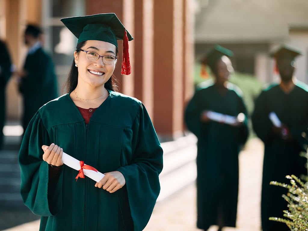 woman at graduation holding diploma in a green cap and gown