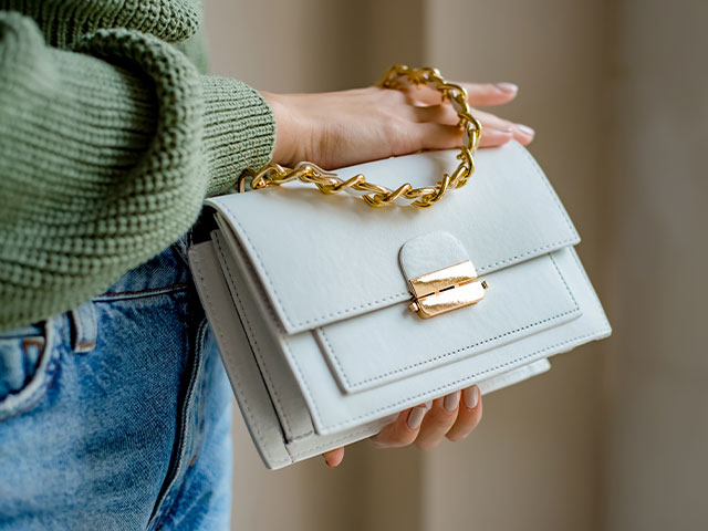 a persons hands holding a small grey clutch purse with a gold chain