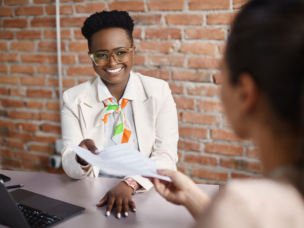 Woman at desk handing colleague information