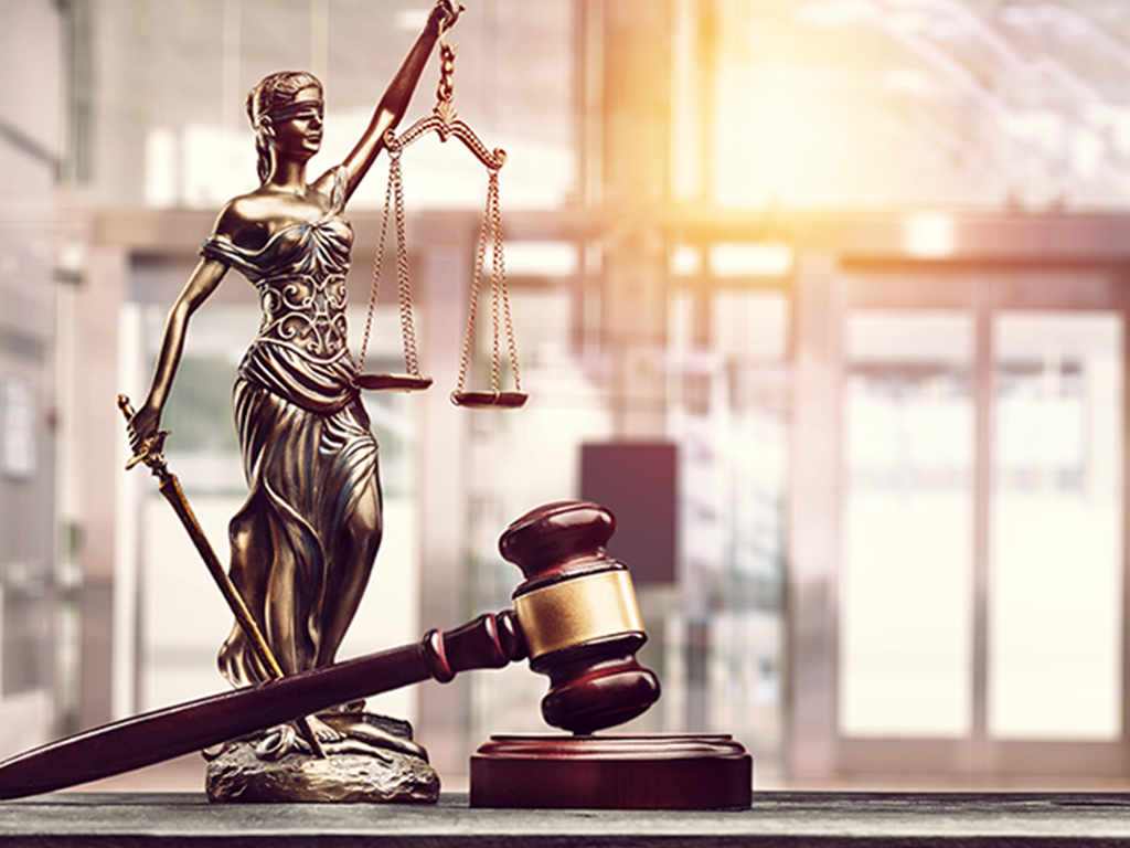  wooden table displaying a judge's gavel and a small statue of "Blind Lady Justice," symbolizing the concept of criminal justice.