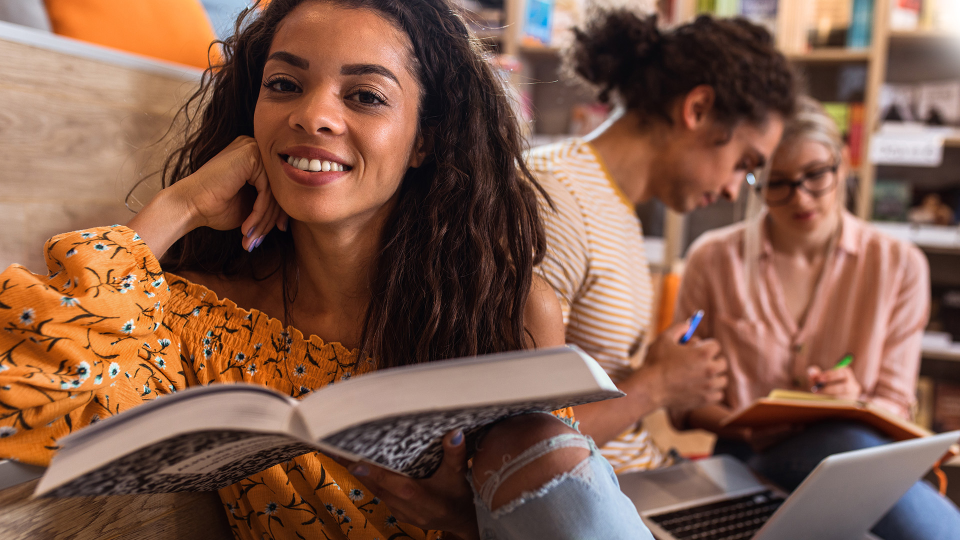 young female student reading a book at a table in the library