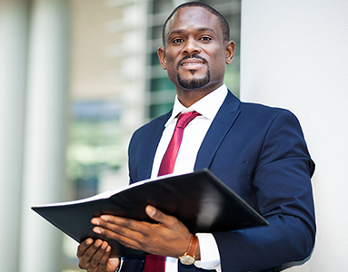  A smiling black male law student holding a book outside of a building