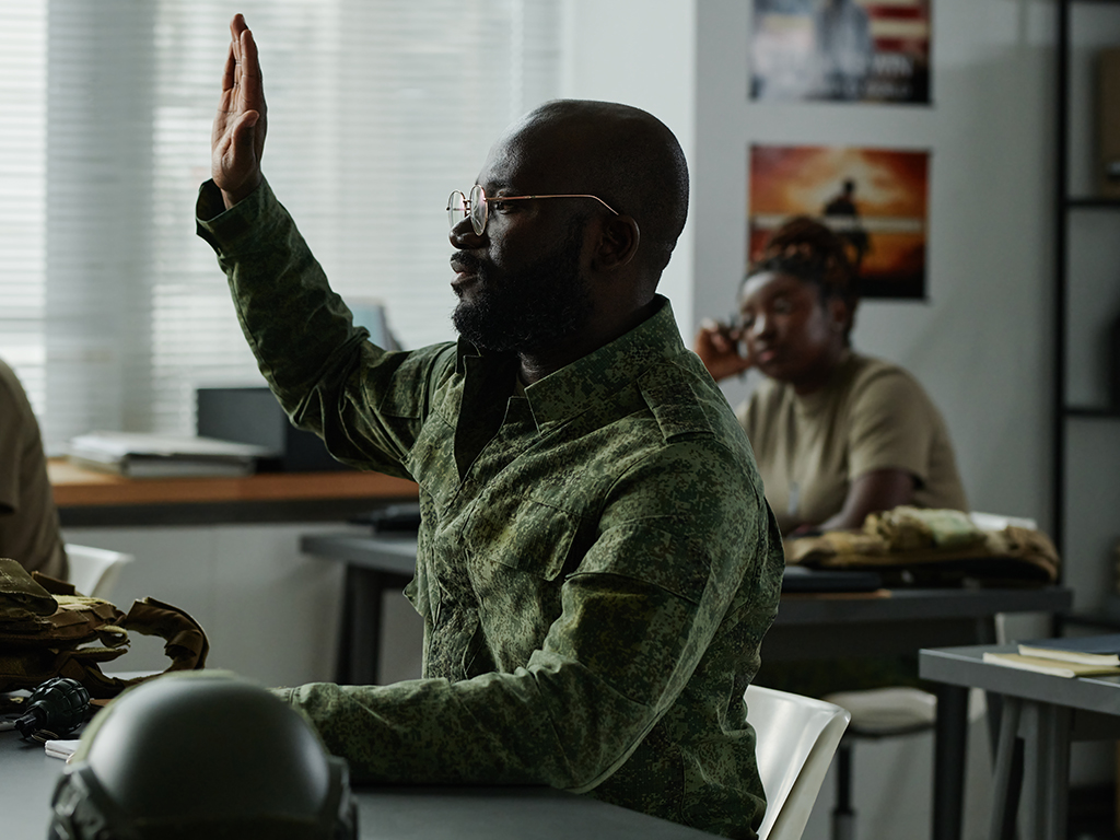 African American guy in military uniform and eyeglasses raising hand and looking at teacher after lecture or presentation to ask question