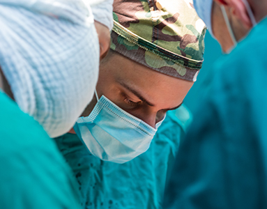 A team of military surgeons in green scrubs and masks performing a surgery in an operating room.