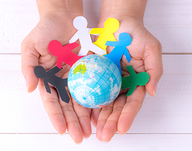 Hands cradling a small globe surrounded by colorful paper cut out people, illustrating unity and interconnectedness worldwide.