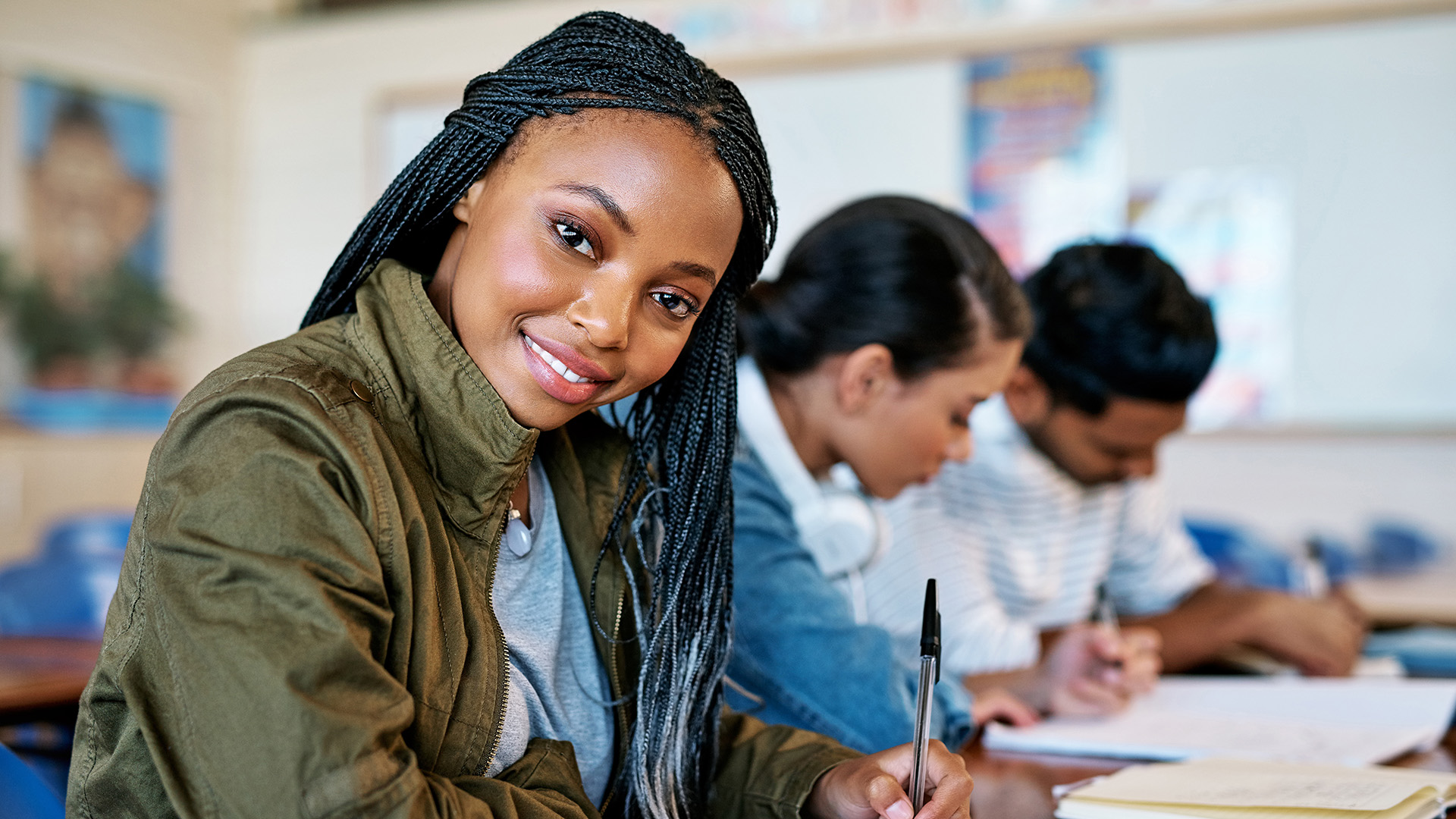 African American female student in classroom. Ahe is smiling and writing something in her notebook.