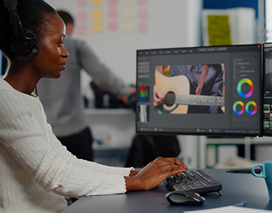  A woman graphic designer intently working on a project, wearing headphones, and sitting in front of a computer.