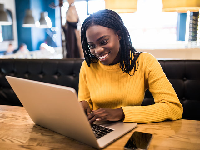 Woman in yellow sweater happily working on laptop