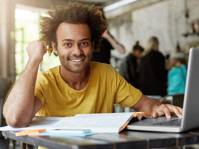 Smiling man with laptop and open books on table.