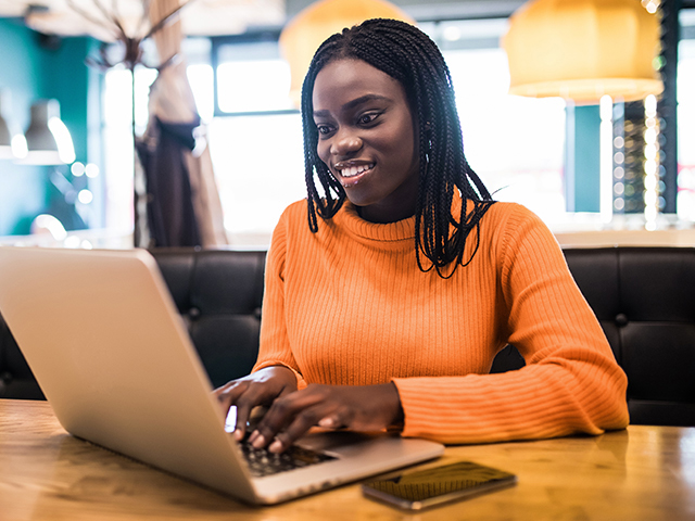 Young woman in orange sweater happily working on laptop