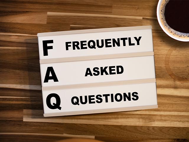 the words "frequently asked questions" on a sign sitting on a wooden desk with a cup of coffee