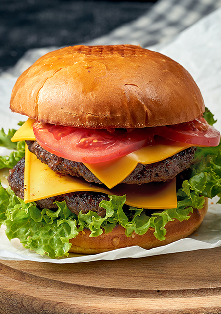 Double burger with beef, tomatoes, lettuce, melted cheese sitting on white parchment paper