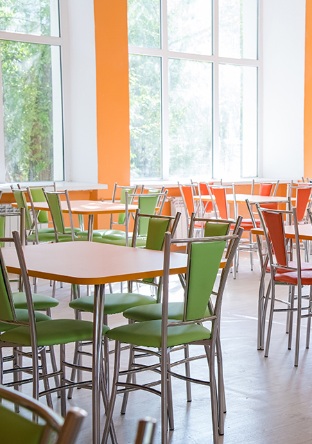 Modern clean campus cafeteria interior with orange and green tables and chairs.