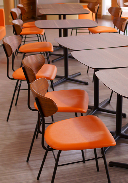 Modern clean campus cafeteria interior with orange and brown wood tables and orange chairs.