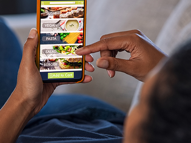 Close up of african american teenager lying on couch using food delivery app on a smartphone.