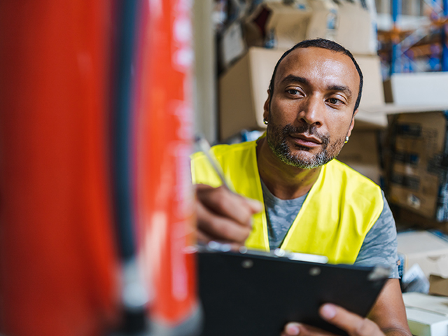 african american worker with pen and clipboard checking and inspecting a fire extinguisher