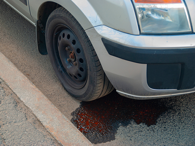 Car on the roadside. Oil is leaking from the engine onto the asphalt below