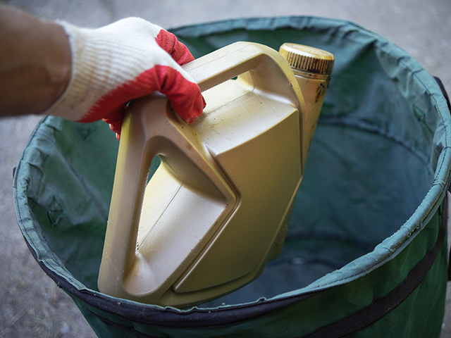 Close up of hand disposing of a bottler of used engine oil