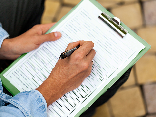 Closeup of an african american person's hands holding a green clipboard and filling out a blank form