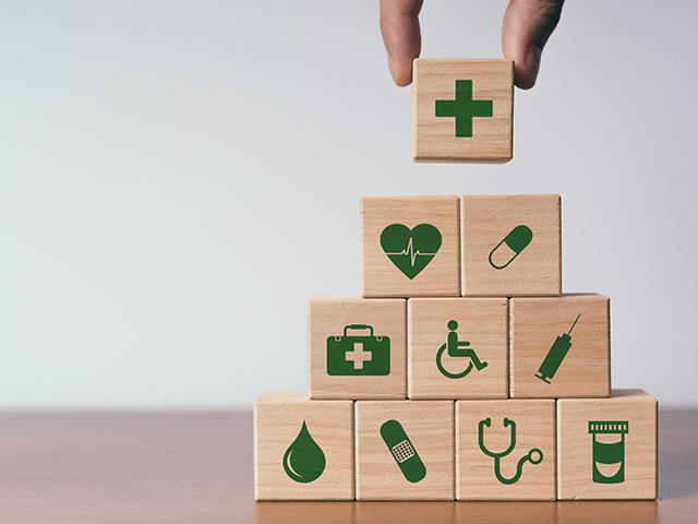 Hand holding a wood block with medical insurance icon on the front over a sack of wood blocks with other medical Insurance icons and motifs on the fronts