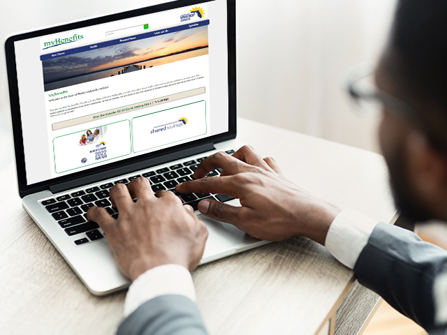 a man sitting at a table with a laptop signing in to the Florida MyBenefits Website