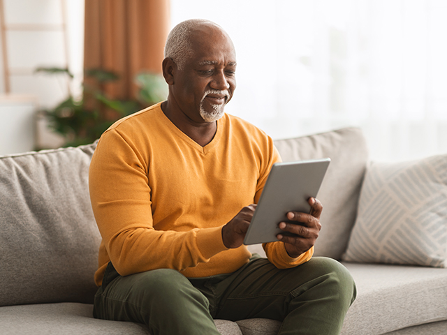 an elderly man sitting on a couch holding an iPad tablet