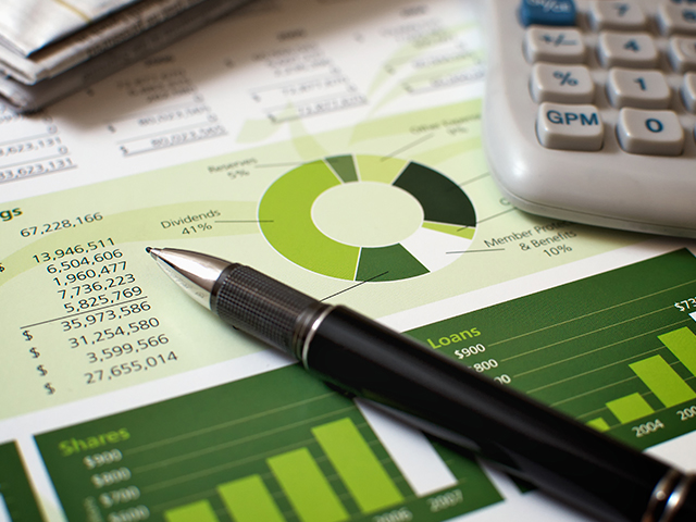 A document with pie charts and bar graphs showing financial reviews or reports. On top of the paper is a writing pen and a calculator.