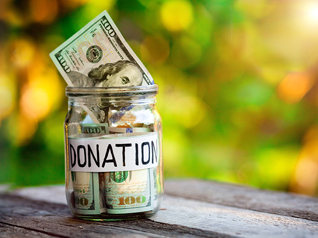 A glass jar full of money in cash. The white label on the jar read "donations" written neatly in black marker