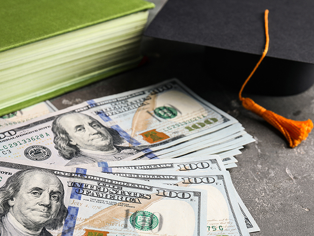 spread of money in cash next to a green book and a graduation cap
