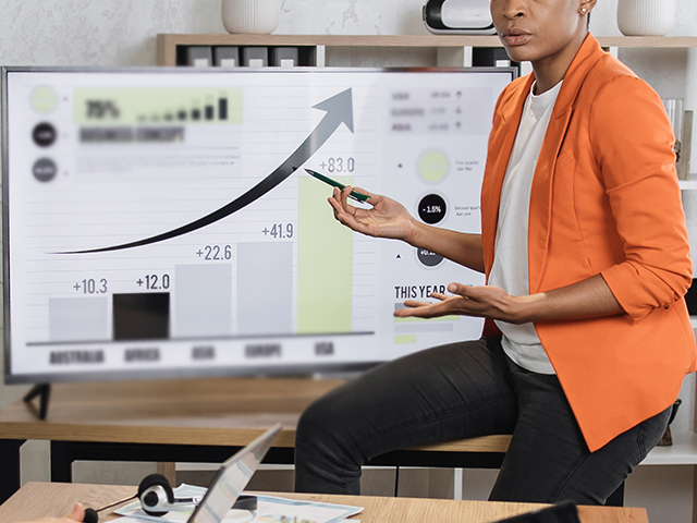 African American woman giving a presentation with monitor that has various graphs and charts