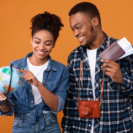 Smiling African American Couple Choosing Travel Destination Holding Globe and Passport Books infront of orange background 
