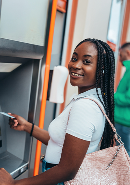 young woman using an ATM, smiling at the camera