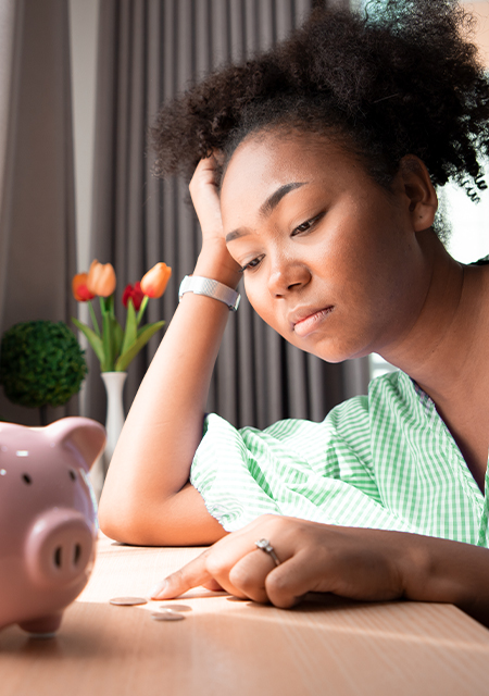 An upset young woman counts coins infront of a piggy bank