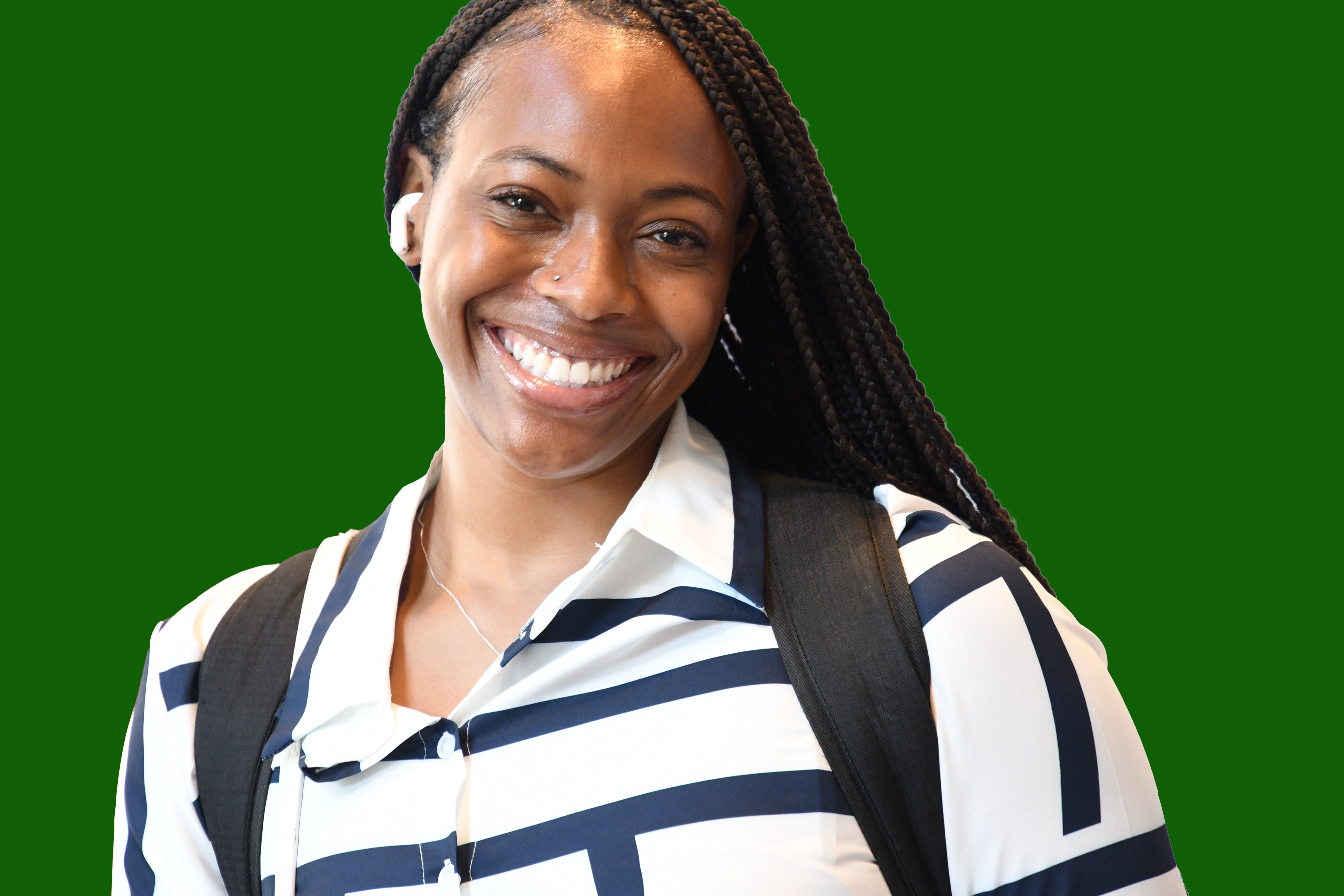 Smiling young African American female student wearing an stripped shirt with backpack on her shoulders. There are three people that are blurred in the background.