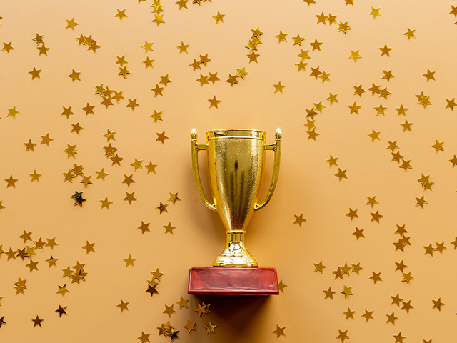 Gold trophy cup on orange background surrounded by shiny star shaped confetti