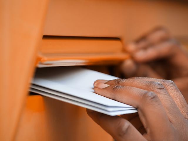Close-up of a person's hand inserting an envelope in an orange outdoor drop box