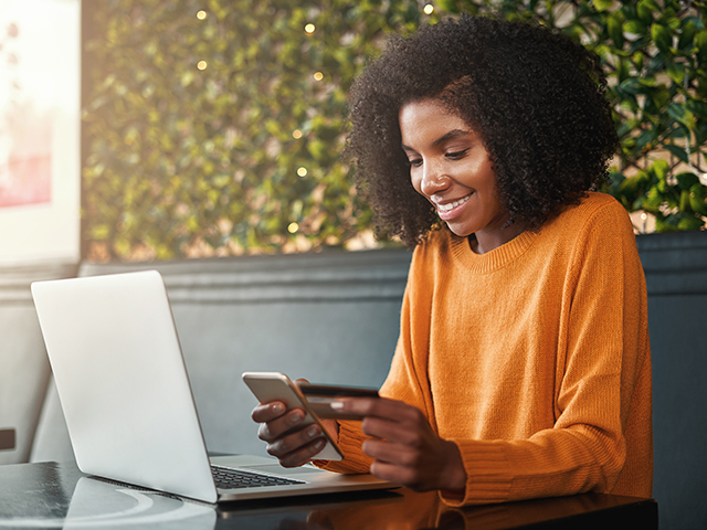 Young African American woman using her phone to make an online payment while holding a credit card