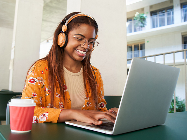 Smiling African American young woman university student in glasses, learning online using laptop computer