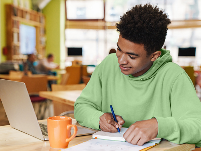 Smiling African American young male university student  learning online using laptop computer and writing notes