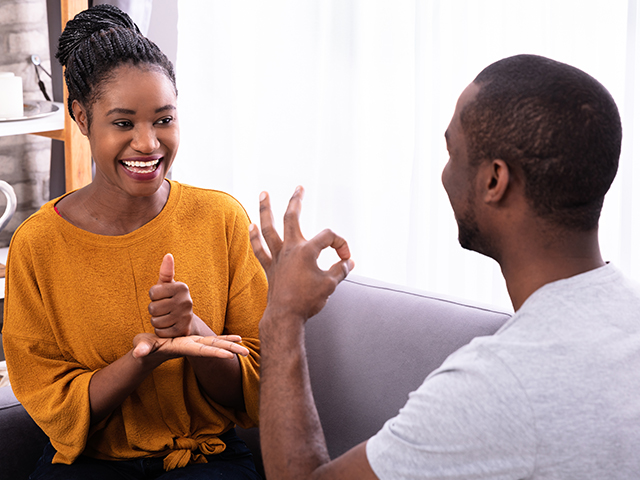 Smiling African-American young man and woman friends Sitting On Sofa Communicating With Sign Language