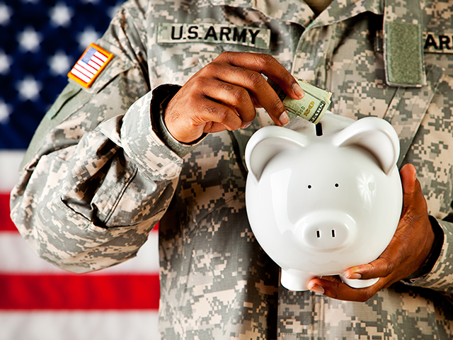 Person in military uniform holdiing aand outting cash into a white piggy ceramic piggy bank