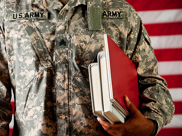Person in military uniform holdiing a stack of books tucked under their arm