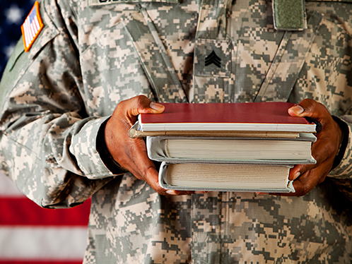 Person in military uniform holdiing a stack of books in front of them