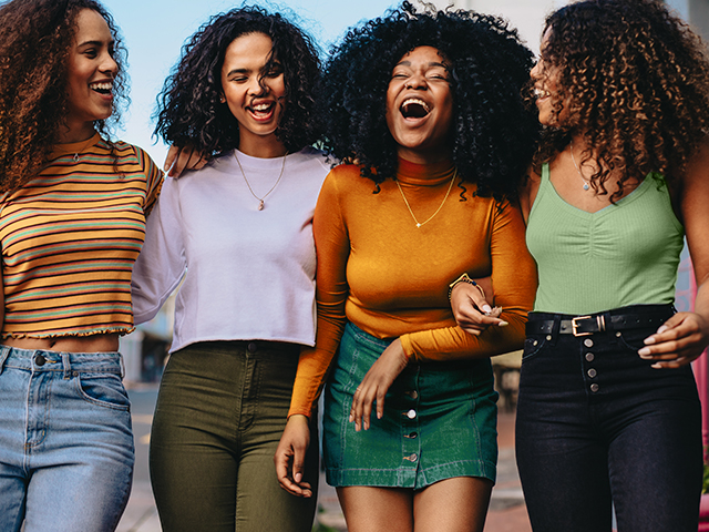 Group of female friends laughing and walking together outdoors in the city.