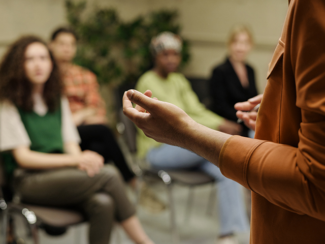 Hands of the presenter standing in front of an audience of young students at seminar while explaining information.